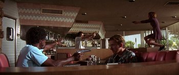 Movie still from “Pulp Fiction” (1994), directed by Quentin Tarantino – A group of people sitting at a table with guns; Medium shot, Over the shoulder angle