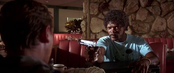 Movie still from “Pulp Fiction” (1994), directed by Quentin Tarantino – A man sitting at a table holding a gun in front of him; Close Up shot, Over the shoulder angle