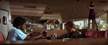 Movie still from “Pulp Fiction” (1994), directed by Quentin Tarantino – Two men sitting at a table with guns in their hands; Medium shot, Over the shoulder angle