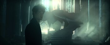 Movie still from “The Sandman” (2022), created by Neil Gaiman – A man standing next to a staircase in a room; Medium shot, Low angle