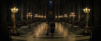 Movie still from “The Sandman” (2022), created by Neil Gaiman – Two women are standing in a large room with lit candles; Extreme Wide shot, High angle