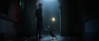 Movie still from “The Sandman” (2022), created by Neil Gaiman – A person standing in the rain with a bird; Wide shot, Low angle