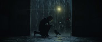 Movie still from “The Sandman” (2022), created by Neil Gaiman – A man kneeling down in front of a black bird; Wide shot, Low angle