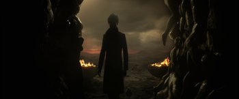 Movie still from “The Sandman” (2022), created by Neil Gaiman – A man standing in front of a fire at night; Wide shot, Over the shoulder angle