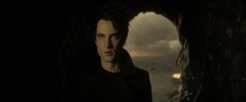 Movie still from “The Sandman” (2022), created by Neil Gaiman – A young man standing under an umbrella on a beach at night; Close Up shot, Low angle