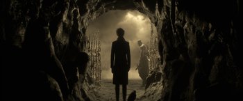 Movie still from “The Sandman” (2022), created by Neil Gaiman – A man standing in front of another man in a cave; Wide shot, Over the shoulder angle