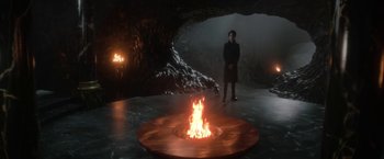 Movie still from “The Sandman” (2022), created by Neil Gaiman – A man standing in front of a fire pit in a cave; Wide shot, High angle