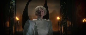 Movie still from “The Sandman” (2022), created by Neil Gaiman – An older woman wearing a white dress and a black umbrella; Medium shot, Low angle