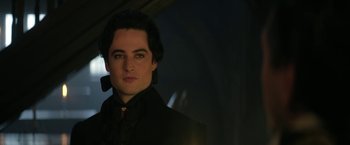 Movie still from “The Sandman” (2022), created by Neil Gaiman – A man in a black suit is looking at the camera; Close Up shot, Low angle