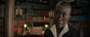 Movie still from “The Sandman” (2022), created by Neil Gaiman – A person with glasses in a room with books; Close Up shot, Over the shoulder angle