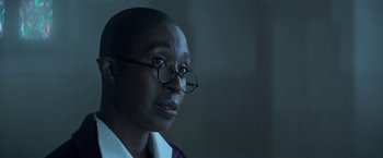 Movie still from “The Sandman” (2022), created by Neil Gaiman – A person wearing glasses and a white shirt; Close Up shot, Over the shoulder angle