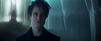 Movie still from “The Sandman” (2022), created by Neil Gaiman – A young man with dark hair is looking at the camera; Close Up shot, Over the shoulder angle