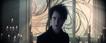 Movie still from “The Sandman” (2022), created by Neil Gaiman – A young man with dark hair is looking at the camera; Close Up shot, Over the shoulder angle