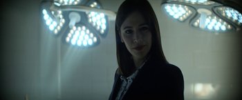 Movie still from “The Sandman” (2022), created by Neil Gaiman – A woman in a black jacket standing next to a wall; Close Up shot, Low angle