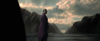 Movie still from “The Sandman” (2022), created by Neil Gaiman – A man in a purple coat standing in front of a body of water; Wide shot, Low angle