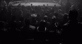 Movie still from “Raging Bull” (1980), directed by Martin Scorsese – A group of people sitting in a boxing ring watching a match; Extreme Wide shot, High angle