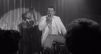 Movie still from “Raging Bull” (1980), directed by Martin Scorsese – A man holding a microphone while sitting next to another man; Medium shot, Low angle