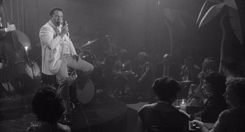 Movie still from “Raging Bull” (1980), directed by Martin Scorsese – A man singing into a microphone on a stage; Medium shot, Over the shoulder angle