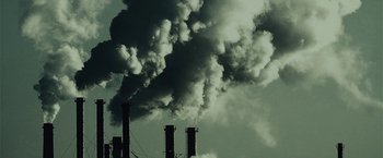Movie still from “The Silence” (2019), directed by John R. Leonetti – Smoke billows out of stacks in front of a cloudy sky; Extreme Wide shot, Low angle