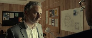 Movie still from “The Silence” (2019), directed by John R. Leonetti – A man standing in front of a bulletin board in an office; Close Up shot, Over the shoulder angle