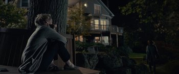 Movie still from “The Silence” (2019), directed by John R. Leonetti – A person sitting on a bench in front of a house; Wide shot, Low angle