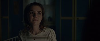 Movie still from “The Silence” (2019), directed by John R. Leonetti – A girl is looking at the camera while sitting in a dark room; Close Up shot, Over the shoulder angle