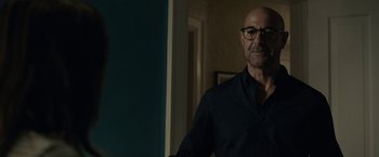 Movie still from “The Silence” (2019), directed by John R. Leonetti – A bald man wearing glasses standing in a room; Medium shot, Over the shoulder angle