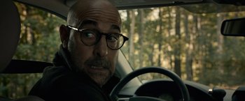 Movie still from “The Silence” (2019), directed by John R. Leonetti – A man with glasses sitting in the driver's seat of a car; Close Up shot, Over the shoulder angle