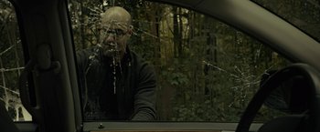Movie still from “The Silence” (2019), directed by John R. Leonetti – A bald man with glasses looking out of a car window; Medium shot, Over the shoulder angle
