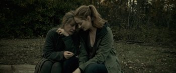 Movie still from “The Silence” (2019), directed by John R. Leonetti – Two women sitting next to each other on the ground; Medium shot, High angle