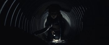 Movie still from “The Silence” (2019), directed by John R. Leonetti – A person is crouched down in a dark tunnel; Medium shot, Low angle
