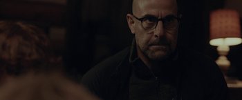 Movie still from “The Silence” (2019), directed by John R. Leonetti – A bald man wearing glasses and a black jacket; Close Up shot, Over the shoulder angle