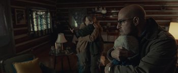 Movie still from “The Silence” (2019), directed by John R. Leonetti – A man and a woman hug in a living room; Medium shot, Over the shoulder angle