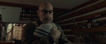 Movie still from “The Silence” (2019), directed by John R. Leonetti – A bald man with glasses holding a pair of socks; Close Up shot, Over the shoulder angle