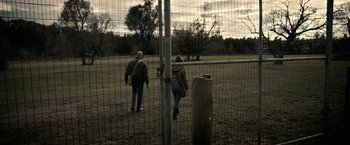 Movie still from “The Silence” (2019), directed by John R. Leonetti – A man and a woman are walking through a fence; Wide shot, Over the shoulder angle