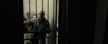 Movie still from “The Silence” (2019), directed by John R. Leonetti – A man standing behind a metal fence looking out of a window; Medium shot, Low angle