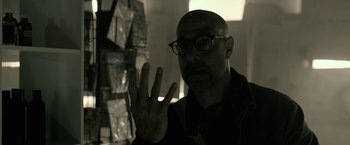 Movie still from “The Silence” (2019), directed by John R. Leonetti – A man with a bald head wearing glasses and a jacket; Close Up shot, Low angle