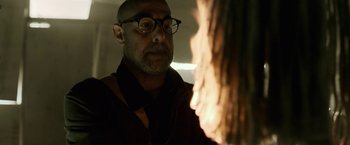 Movie still from “The Silence” (2019), directed by John R. Leonetti – A bald man with glasses looking at a fire; Close Up shot, Low angle