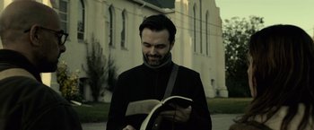 Movie still from “The Silence” (2019), directed by John R. Leonetti – A man is reading a book on the sidewalk; Close Up shot, Low angle
