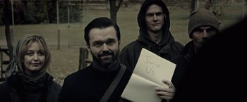 Movie still from “The Silence” (2019), directed by John R. Leonetti – A man holding a sign next to another man; Close Up shot, High angle