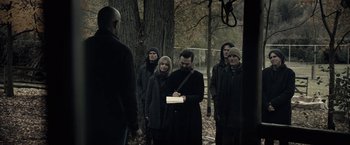 Movie still from “The Silence” (2019), directed by John R. Leonetti – A group of people standing around a tree in the woods; Medium shot, Over the shoulder angle