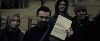 Movie still from “The Silence” (2019), directed by John R. Leonetti – A man holding up a sign that says " join us " while another man holds up a sign that says " follow our example "; Close Up shot, High angle