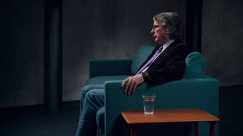Movie still from “The Social Dilemma” (2020), directed by Jeff Orlowski-Yang – A man sitting on a couch next to a glass of water; Medium shot, High angle