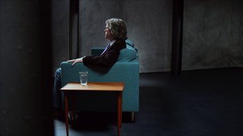 Movie still from “The Social Dilemma” (2020), directed by Jeff Orlowski-Yang – A person sitting in a chair next to a small table; Wide shot, Over the shoulder angle