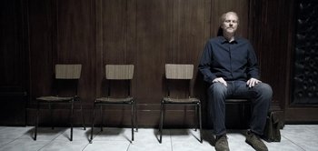 Movie still from “The Spy” (2019), directed by Gideon Raff – A man sitting in front of a row of chairs; Medium shot, Low angle