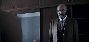 Movie still from “The Spy” (2019), directed by Gideon Raff – A man with a beard wearing a suit and tie; Medium shot, Over the shoulder angle