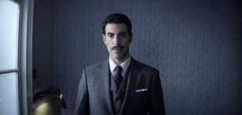 Movie still from “The Spy” (2019), directed by Gideon Raff – A man in a suit and tie standing in front of a wall; Close Up shot, Low angle