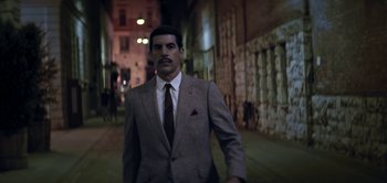Movie still from “The Spy” (2019), directed by Gideon Raff – A man in a suit and tie standing in a street; Medium shot, Low angle