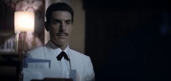 Movie still from “The Spy” (2019), directed by Gideon Raff – A man wearing a white suit and a black tie; Close Up shot, Over the shoulder angle