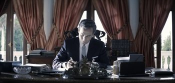 Movie still from “The Spy” (2019), directed by Gideon Raff – A man sitting at a desk writing on a piece of paper; Medium shot, Low angle